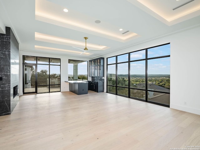 unfurnished living room featuring a raised ceiling, floor to ceiling windows, a fireplace, and light hardwood / wood-style flooring