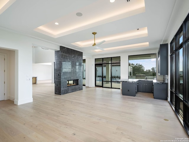 unfurnished living room featuring sink, ceiling fan, light wood-type flooring, a fireplace, and a tray ceiling