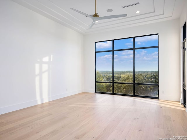 empty room with a raised ceiling, ceiling fan, and light hardwood / wood-style floors