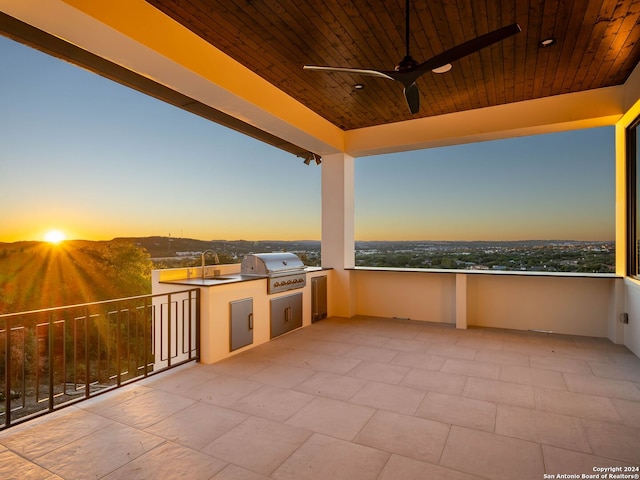 patio terrace at dusk with ceiling fan, a grill, a balcony, and sink