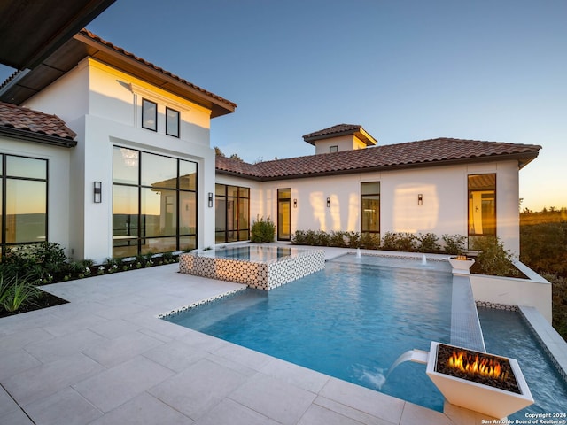 pool at dusk with pool water feature, a fire pit, an in ground hot tub, and a patio