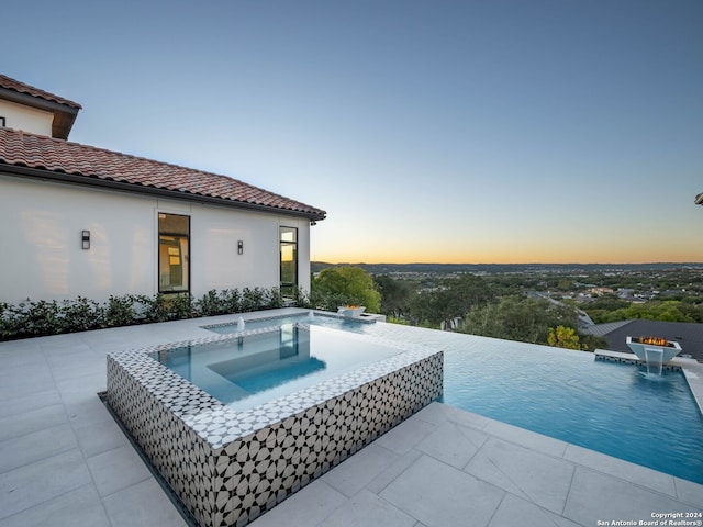 pool at dusk with pool water feature and an in ground hot tub