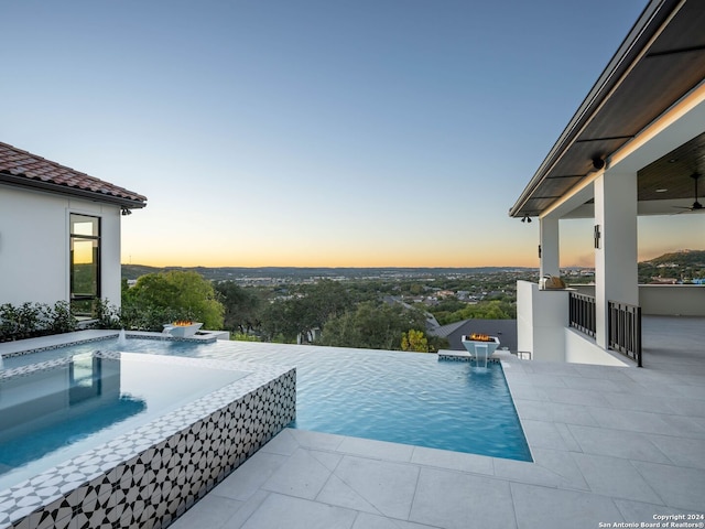 pool at dusk with pool water feature, ceiling fan, and a patio