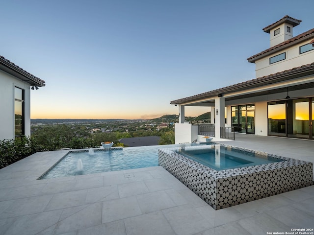 pool at dusk featuring pool water feature, an in ground hot tub, and a patio