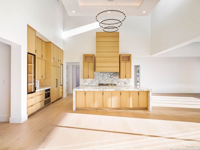 kitchen featuring kitchen peninsula, light brown cabinets, a towering ceiling, and a chandelier