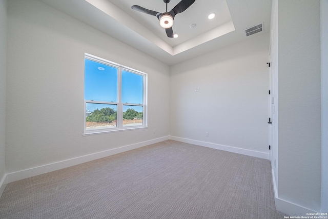 spare room with ceiling fan, carpet floors, and a tray ceiling