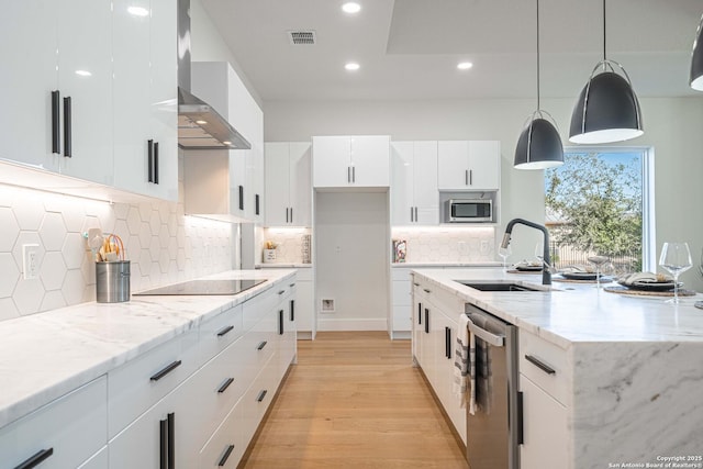 kitchen featuring wall chimney exhaust hood, stainless steel appliances, sink, decorative light fixtures, and white cabinets