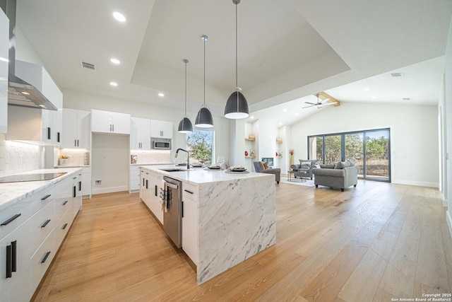 kitchen with white cabinets, lofted ceiling with beams, an island with sink, decorative light fixtures, and stainless steel appliances