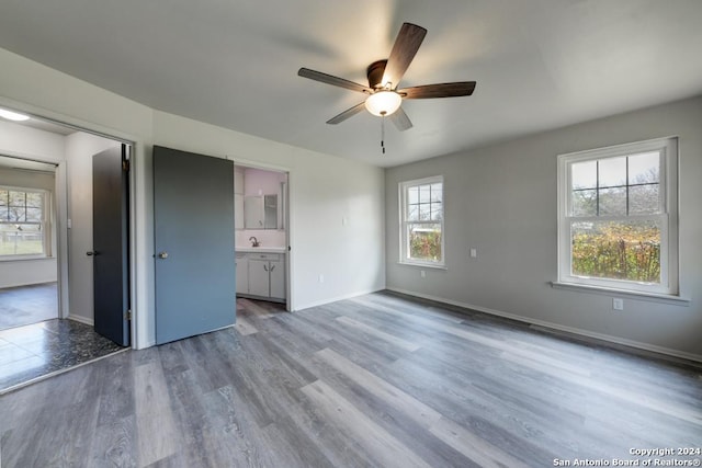 unfurnished bedroom featuring hardwood / wood-style flooring, ceiling fan, connected bathroom, and multiple windows