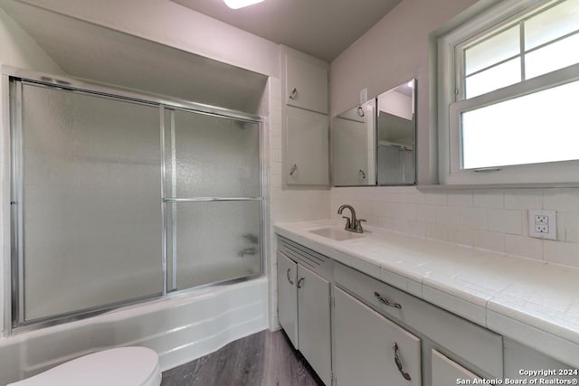 full bathroom with hardwood / wood-style floors, vanity, backsplash, combined bath / shower with glass door, and toilet