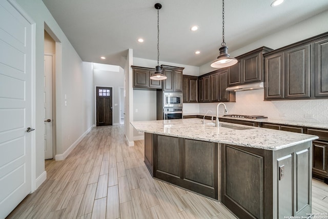 kitchen featuring dark brown cabinetry, stainless steel appliances, decorative light fixtures, light hardwood / wood-style flooring, and an island with sink