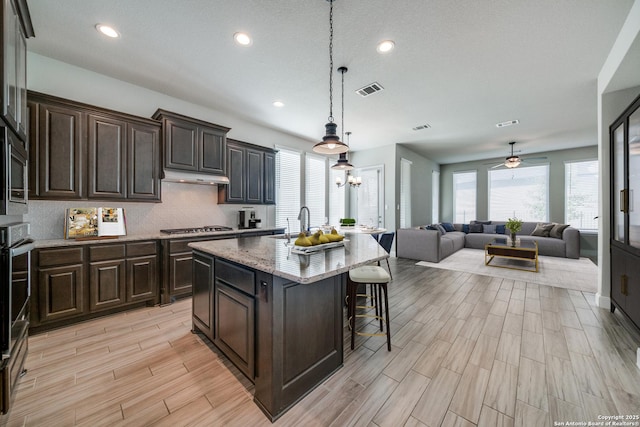 kitchen with ceiling fan, tasteful backsplash, decorative light fixtures, a center island with sink, and appliances with stainless steel finishes