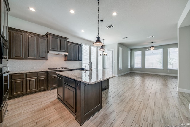 kitchen featuring ceiling fan, sink, stainless steel appliances, hanging light fixtures, and a kitchen island with sink