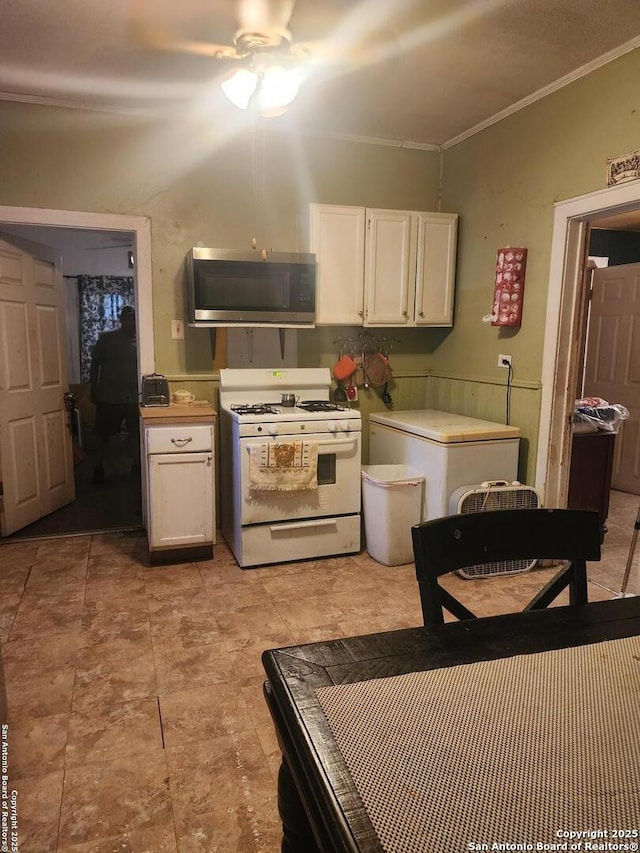 kitchen featuring refrigerator, ceiling fan, crown molding, white range with gas stovetop, and white cabinetry