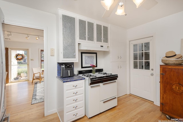 kitchen with ventilation hood, white gas range oven, light hardwood / wood-style flooring, ceiling fan, and white cabinetry