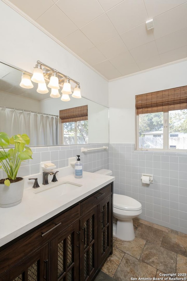 bathroom with vanity, a healthy amount of sunlight, crown molding, and tile walls