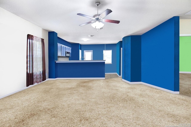 unfurnished living room featuring carpet, ceiling fan, and sink