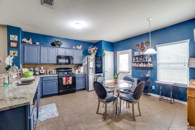 kitchen with sink, light stone counters, pendant lighting, light tile patterned floors, and black appliances