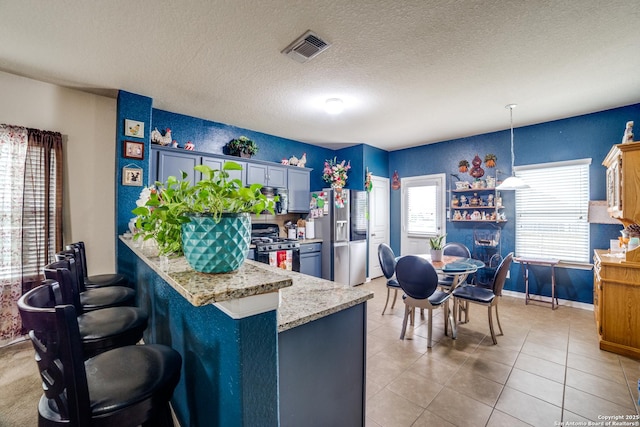 kitchen featuring black gas stove, stainless steel fridge, decorative light fixtures, kitchen peninsula, and a breakfast bar area