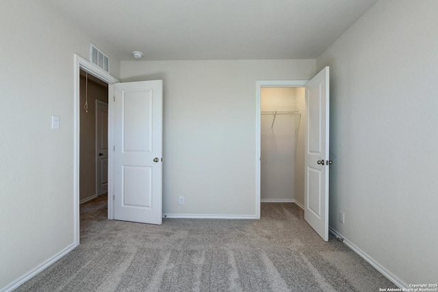 unfurnished bedroom featuring a walk in closet, a closet, and light colored carpet