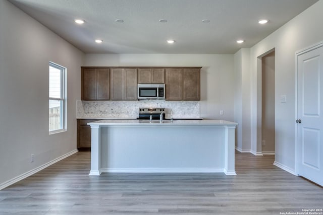 kitchen with sink, appliances with stainless steel finishes, backsplash, and an island with sink