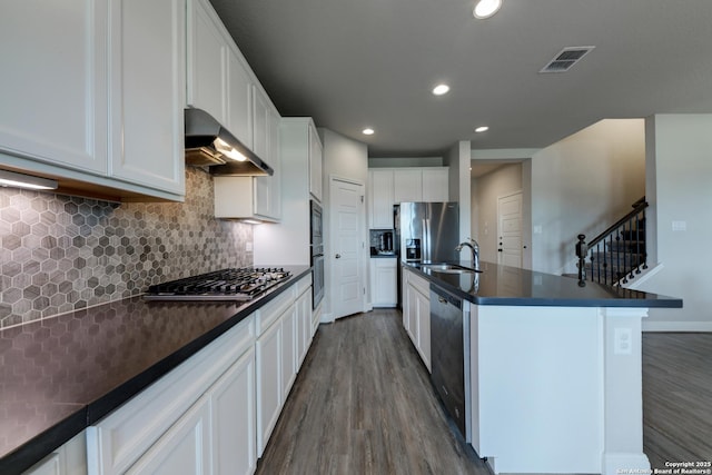 kitchen featuring white cabinetry, wall chimney exhaust hood, dark wood-type flooring, an island with sink, and appliances with stainless steel finishes