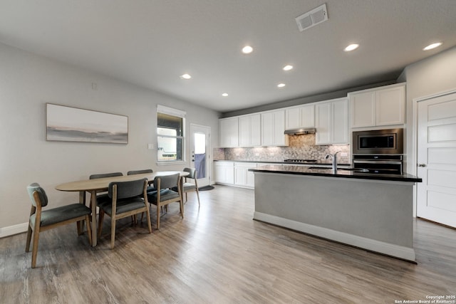 kitchen with a center island with sink, sink, appliances with stainless steel finishes, light hardwood / wood-style floors, and white cabinetry