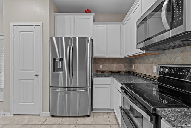 kitchen with appliances with stainless steel finishes, tasteful backsplash, light tile patterned floors, dark stone countertops, and white cabinetry