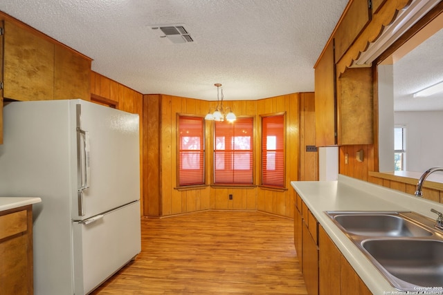 kitchen featuring sink, decorative light fixtures, wooden walls, a notable chandelier, and white fridge