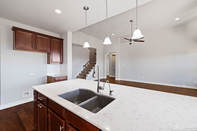 kitchen with dark wood-type flooring, sink, light stone countertops, tasteful backsplash, and decorative light fixtures