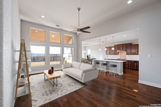 living room with dark hardwood / wood-style floors, ceiling fan, sink, and a high ceiling