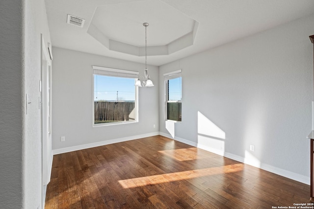 unfurnished dining area featuring hardwood / wood-style floors, a notable chandelier, and a tray ceiling