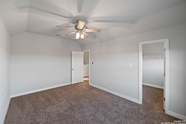 unfurnished bedroom with ceiling fan, vaulted ceiling, a walk in closet, a closet, and dark carpet