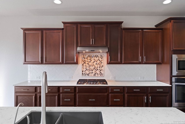 kitchen featuring backsplash, light stone counters, sink, and appliances with stainless steel finishes