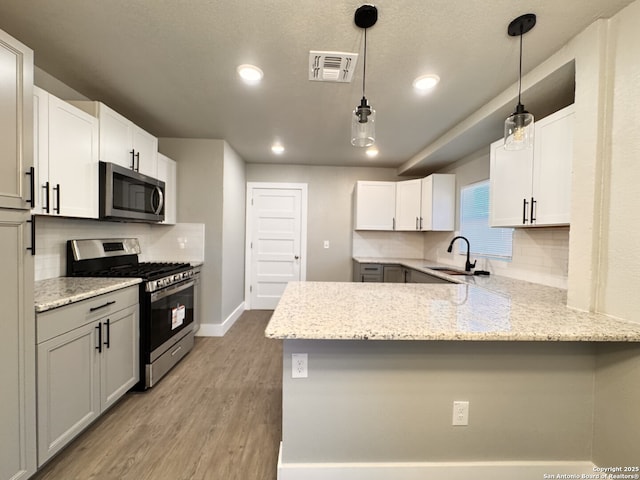 kitchen with kitchen peninsula, appliances with stainless steel finishes, sink, white cabinets, and hanging light fixtures