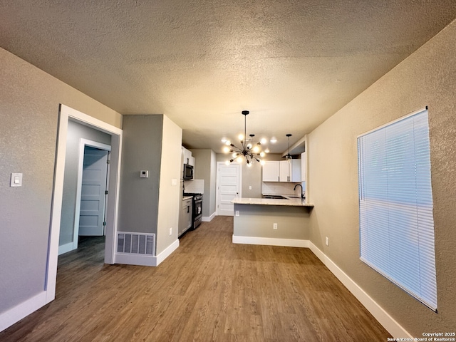 kitchen with white cabinets, kitchen peninsula, decorative light fixtures, wood-type flooring, and a chandelier