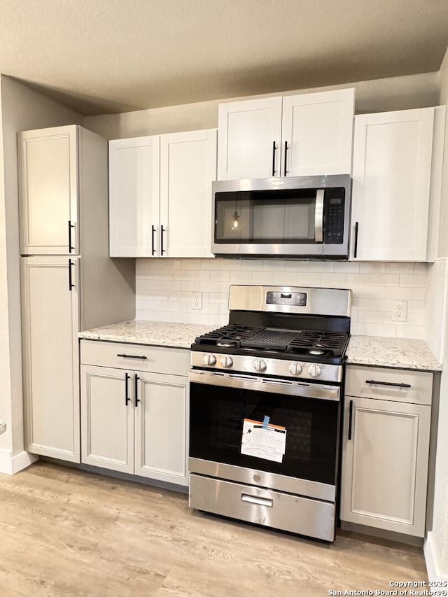 kitchen with light stone countertops, light wood-type flooring, stainless steel appliances, and white cabinetry