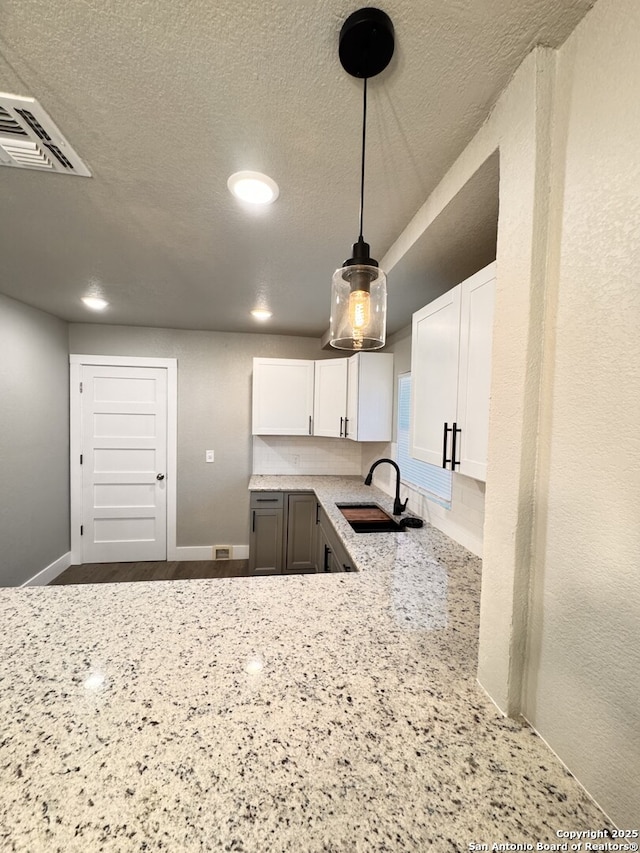 kitchen featuring pendant lighting, sink, a textured ceiling, light stone counters, and white cabinetry