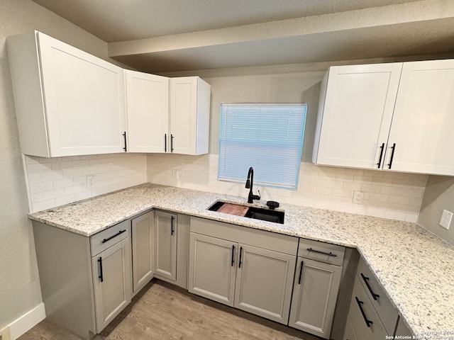 kitchen featuring light stone countertops, decorative backsplash, light hardwood / wood-style flooring, and sink