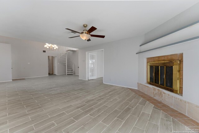 unfurnished living room featuring a tile fireplace and ceiling fan with notable chandelier