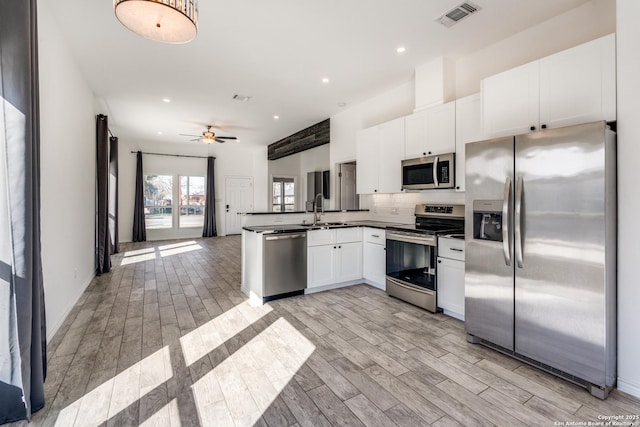 kitchen with sink, ceiling fan, appliances with stainless steel finishes, white cabinetry, and kitchen peninsula