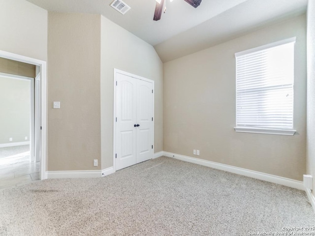 unfurnished bedroom featuring a closet, light colored carpet, vaulted ceiling, and ceiling fan