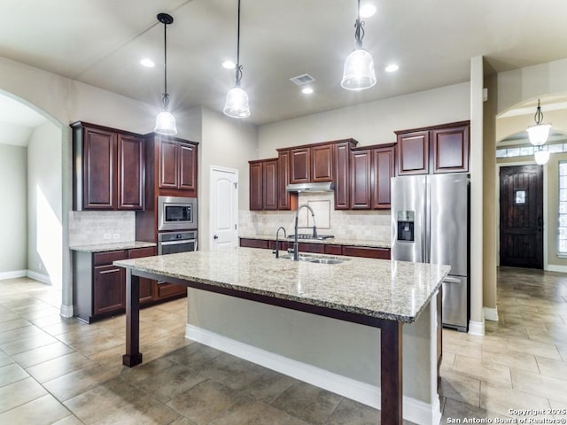 kitchen with light stone countertops, tasteful backsplash, stainless steel appliances, sink, and an island with sink