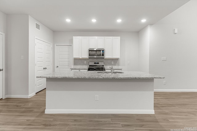 kitchen featuring light stone counters, a center island with sink, white cabinets, and stainless steel appliances