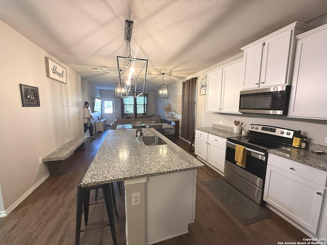 kitchen with stainless steel appliances, sink, a center island with sink, white cabinets, and hanging light fixtures