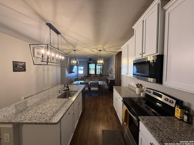 kitchen featuring white cabinets, a center island with sink, sink, appliances with stainless steel finishes, and decorative light fixtures