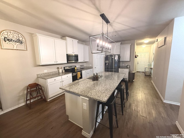 kitchen featuring stainless steel appliances, a kitchen breakfast bar, an island with sink, pendant lighting, and white cabinets