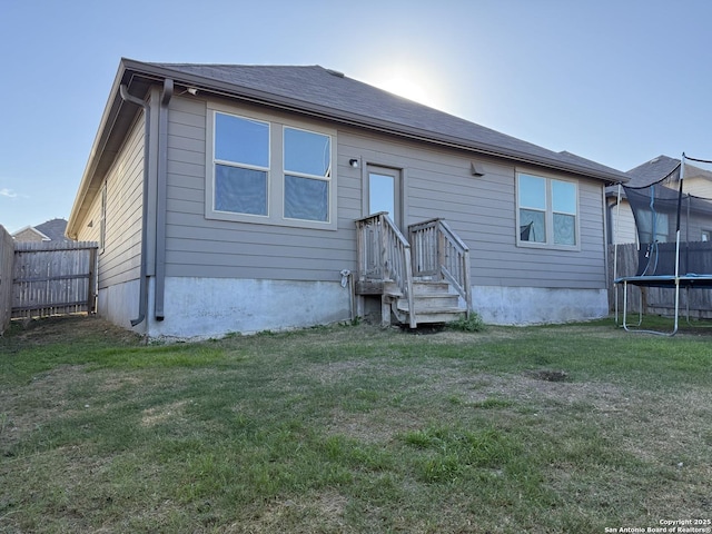 back of property featuring a lawn and a trampoline