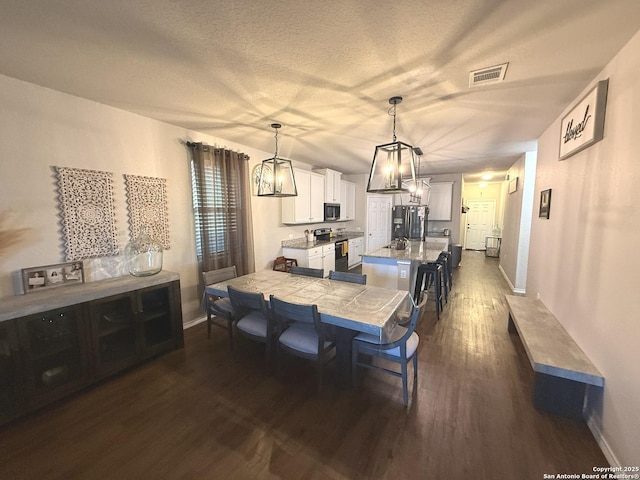 dining space featuring dark wood-type flooring, a textured ceiling, and an inviting chandelier