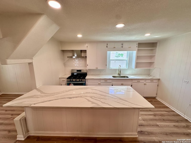 kitchen featuring stainless steel gas range oven, a textured ceiling, sink, wall chimney range hood, and white cabinetry